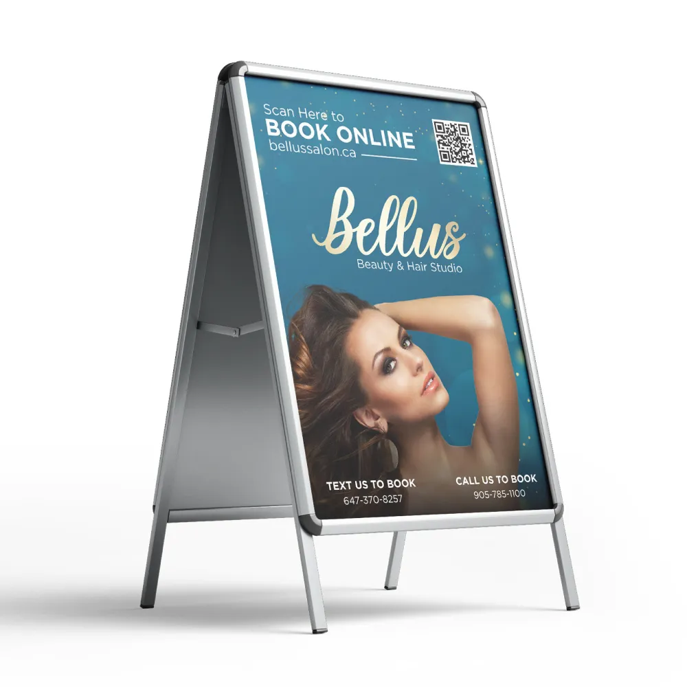 A sidewalk A-frame advertising sign for Bellus Beauty & Hair Studio, featuring their logo, a professional beauty photo, QR code for online booking at bellussalon.ca, and contact information for booking via text or phone. The sign has an aluminum frame with a teal-colored promotional poster.