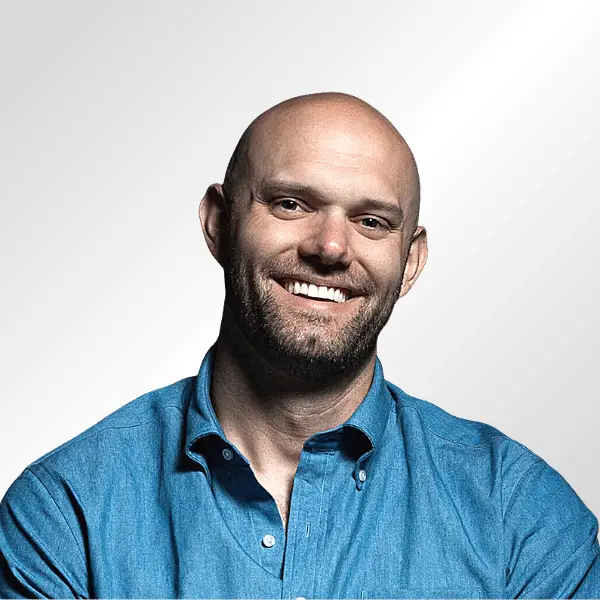 Smiling bald man with a beard wearing a blue button-up shirt against a light gradient background.