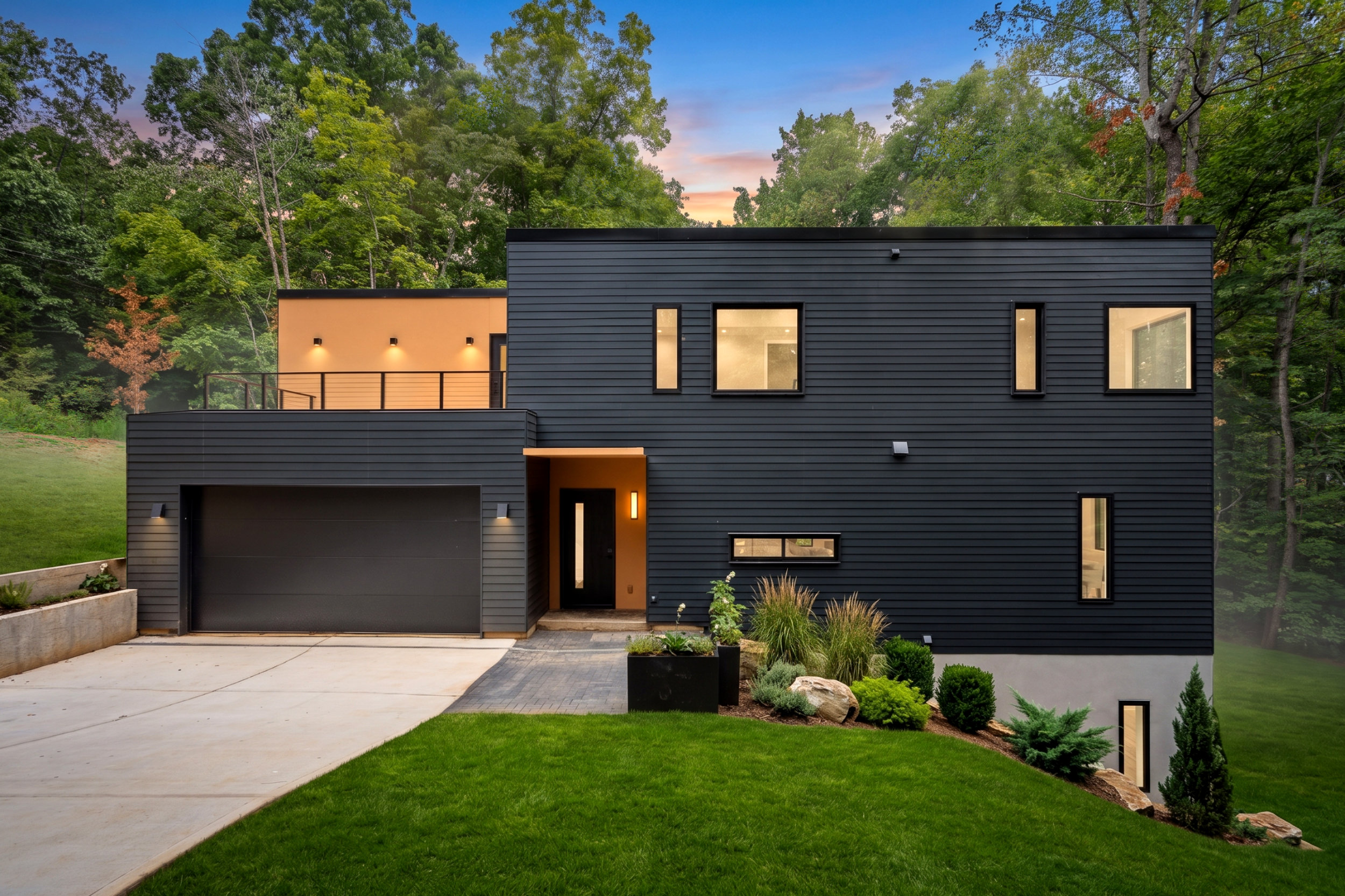 Modern two-story house with dark horizontal siding, large windows, a black garage door, and a beige accent wall surrounded by trees.