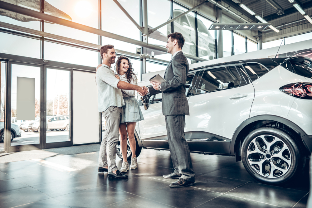 Young couple shaking hands with sales agent after successfully buying a car.