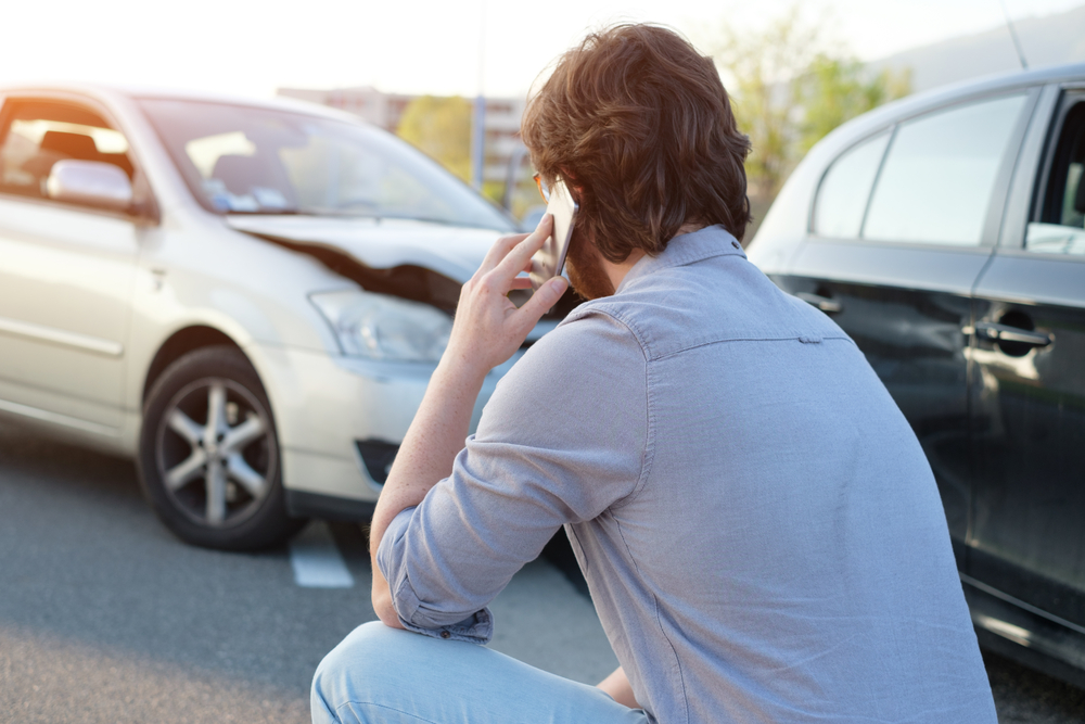 A man calls his insurance company on a cell phone after a minor accident.