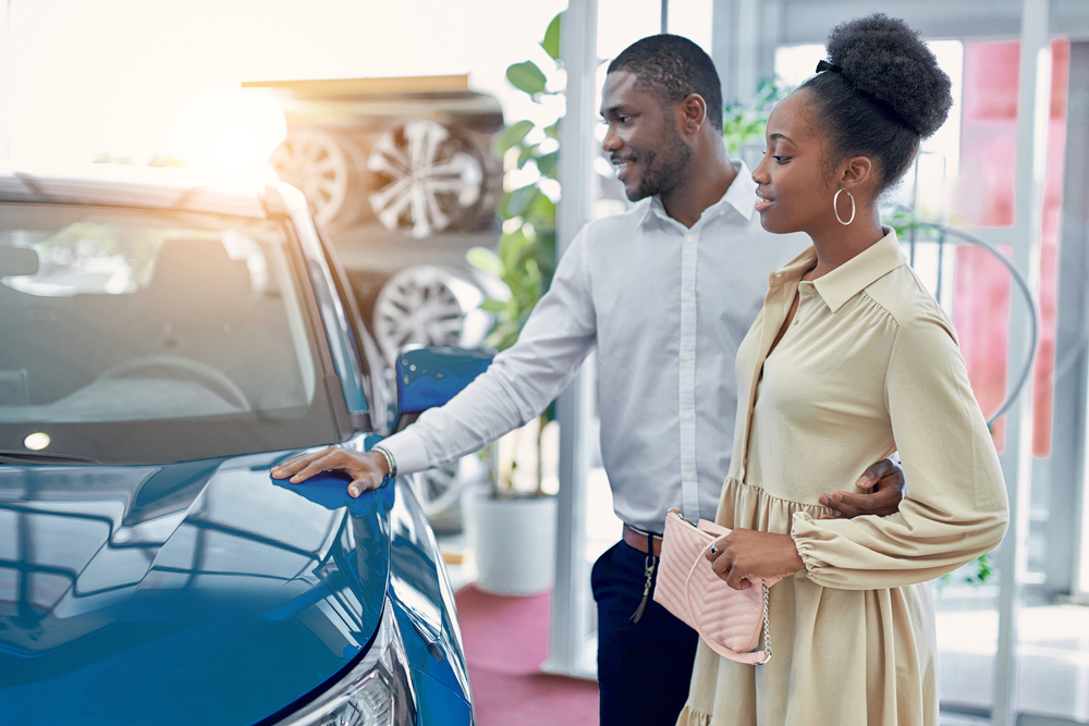 A man and woman examine a blue car at a car dealership