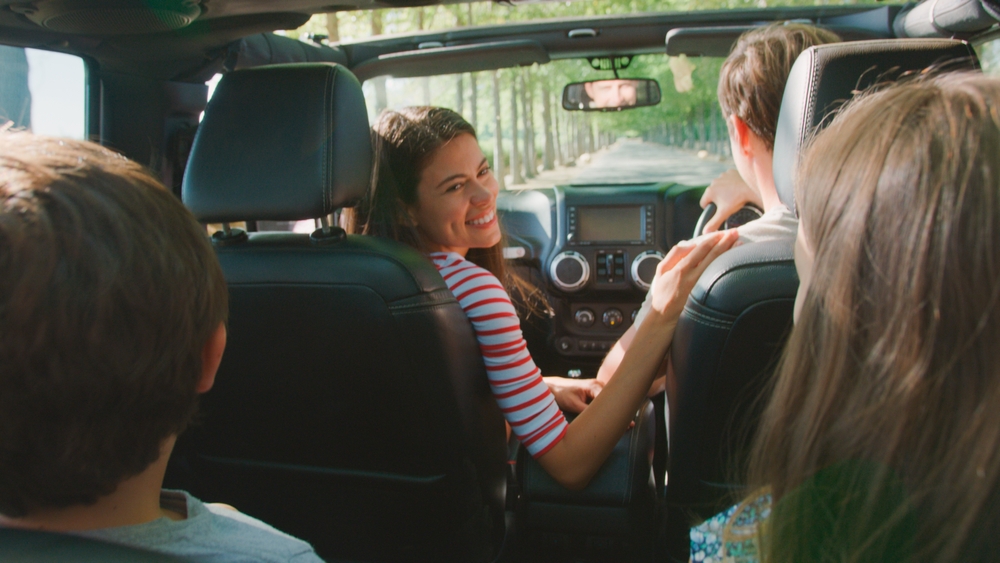 View from car backseat as dad sits in passenger seat and mom turns back to look at two children 