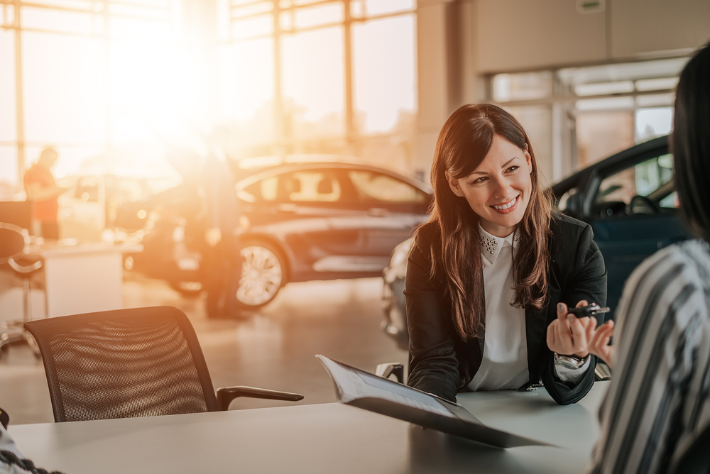 Saleswoman hands over car keys to driver while reviewing paperwork of lease buyout fees