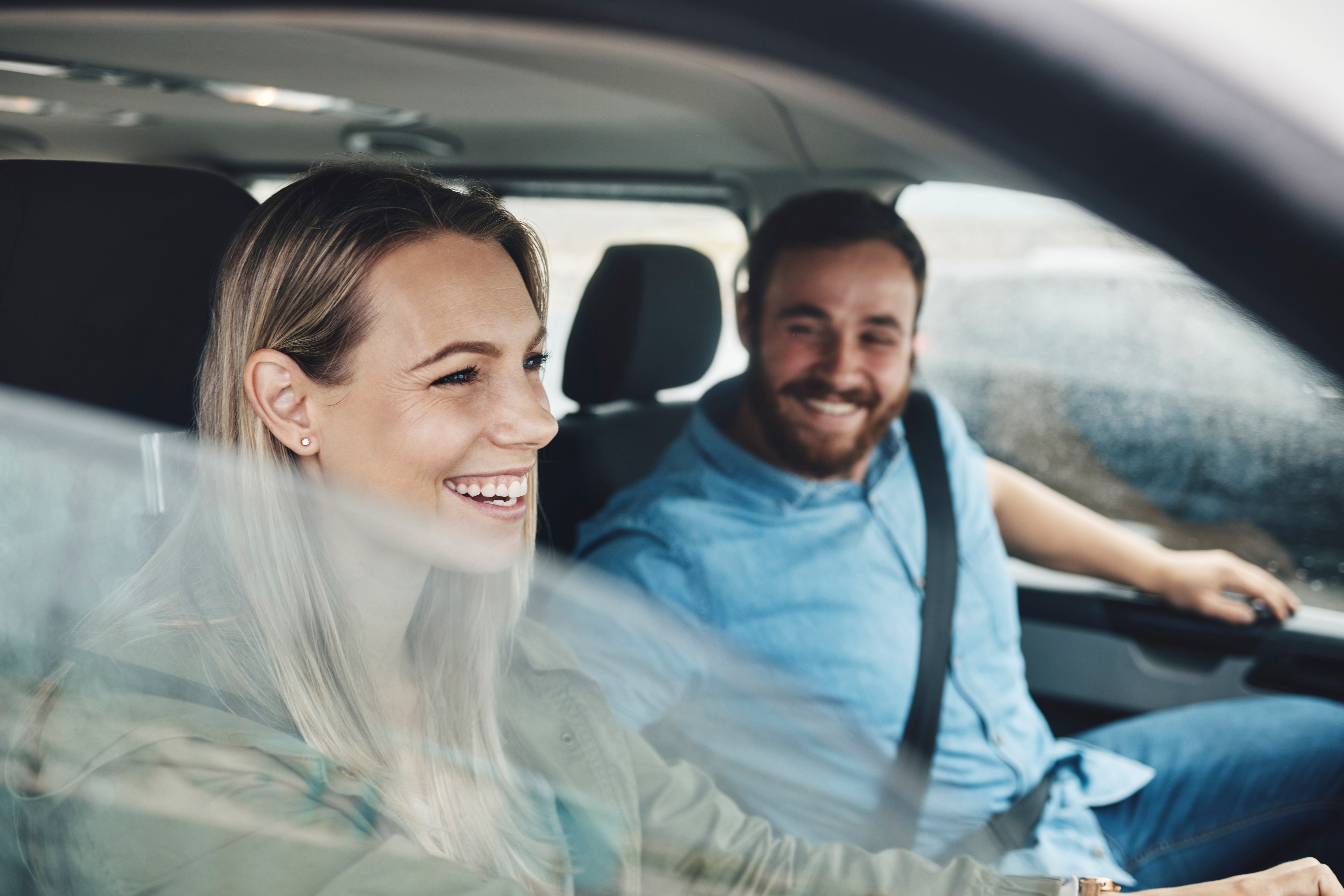 A woman sitting in the passenger seat of a car and smiles at her friend, who is in the driver’s seat.