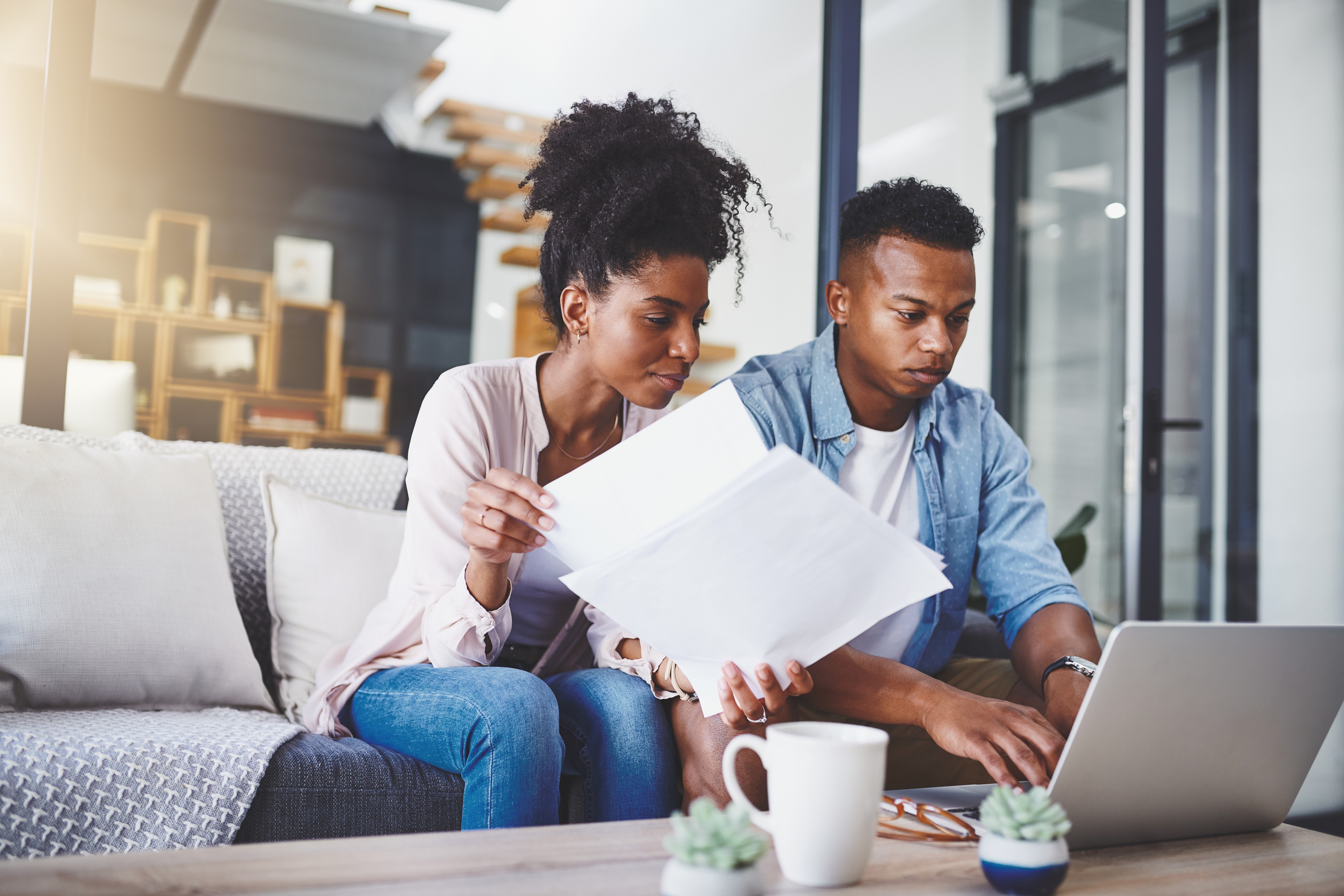 A man and a woman sit side-by-side on a sofa at home, reviewing their credit reports, an open laptop on the table in front of them