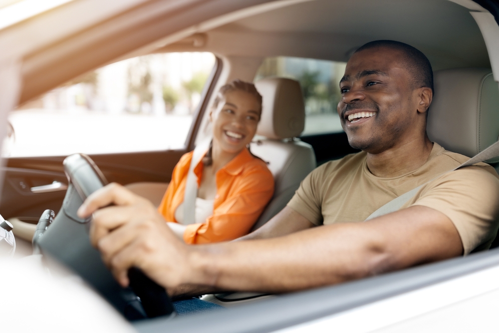 A smiling man driving a Honda with a smiling woman in the passenger seat. 
