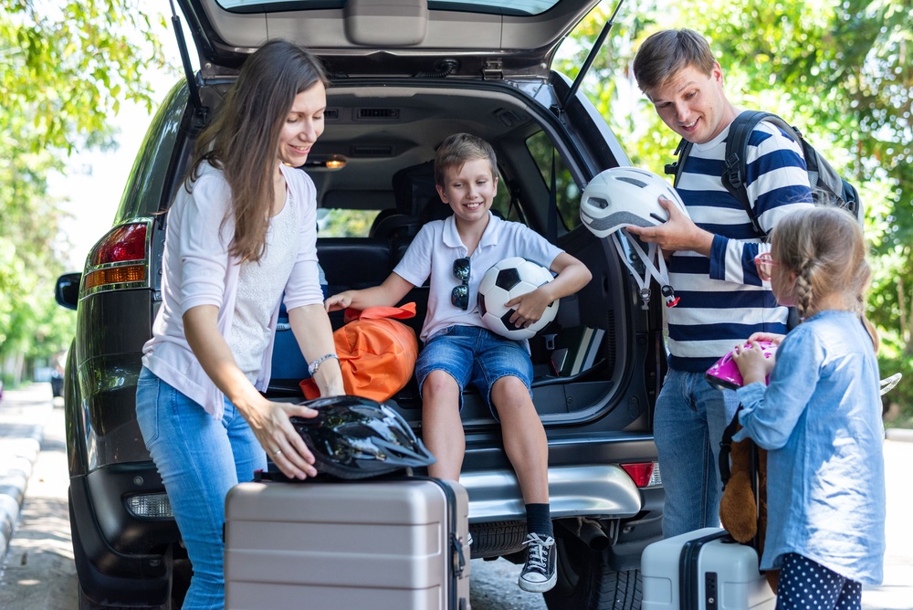 A family of four unloads sports gear and luggage from their leased SUV.