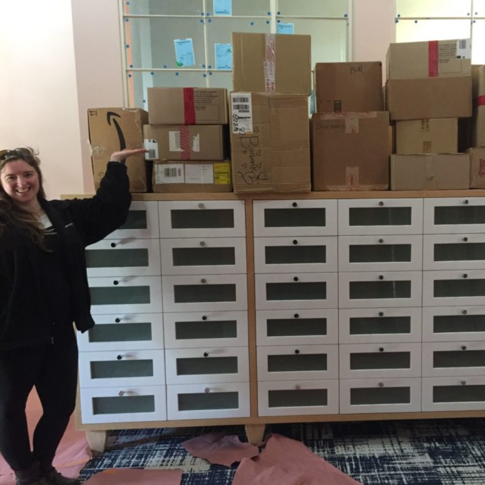 A woman standing in front of a dresser piled with cardboard boxes