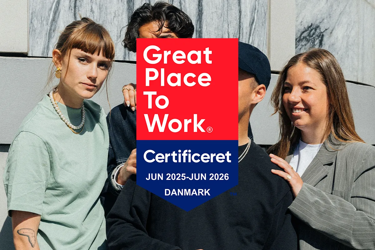 Tre unge mennesker står sammen foran en marmorbagtæppe med et Great Place To Work certificeringslogo overlagt.