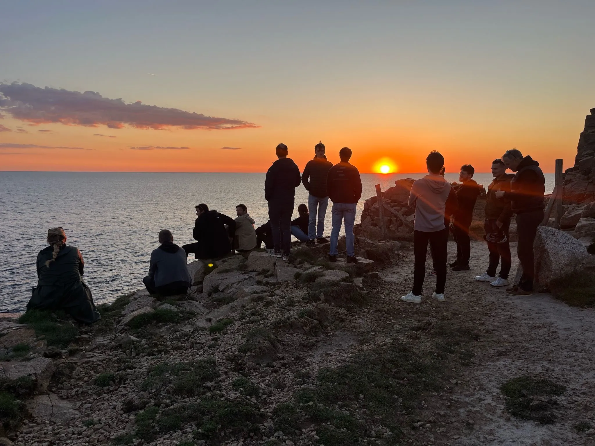 Group of people watching a sunset over the ocean from rocky cliffs.