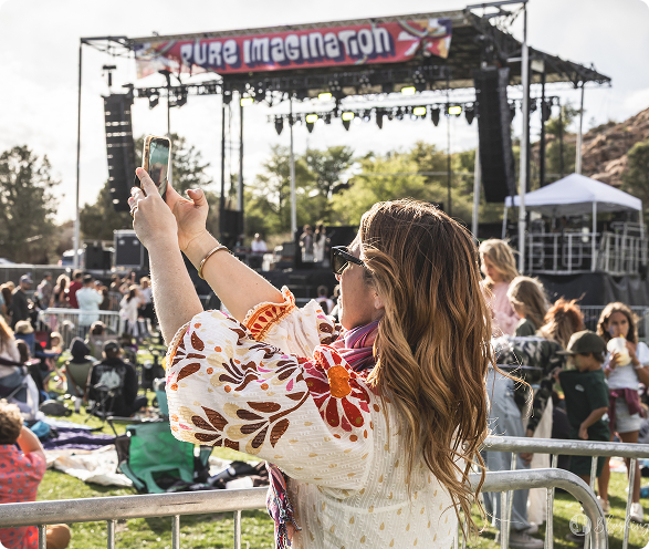A woman with floral sleeves takes a selfie at an outdoor music festival named Pure Imagination.