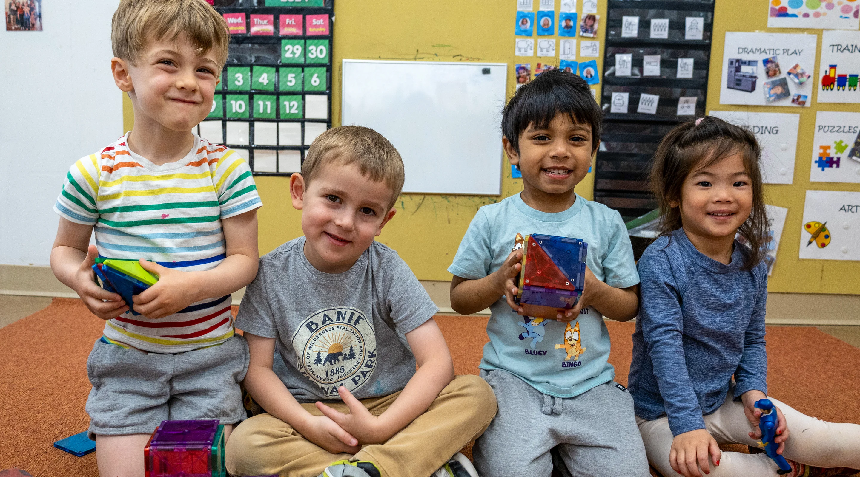 Four children sit in a row in a classroom, posing for a group portrait.