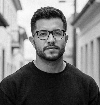 Man with glasses and beard taking a black-and-white selfie holding a smartphone.