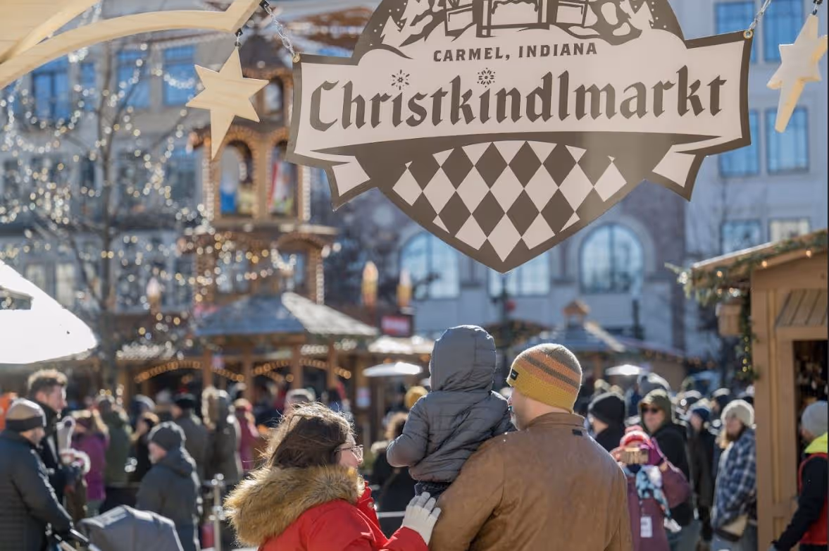 Family with a child at Carmel, Indiana Christkindlmarkt Christmas market with festive lights and crowd.