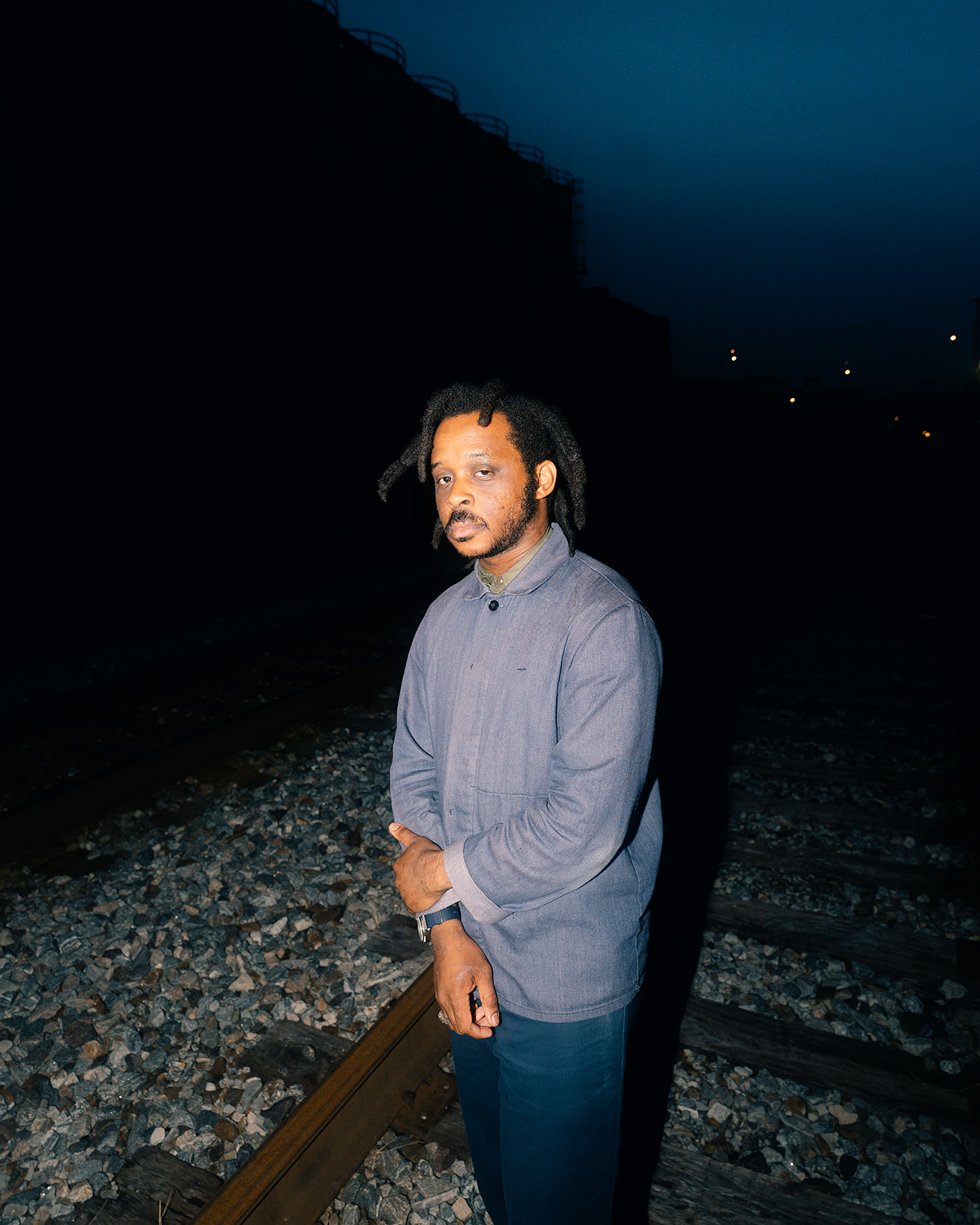 Curry J. Hackett's headshot. He's an attractive Black American man with thick locs, wearing an light jacket over a patterned shirt.
