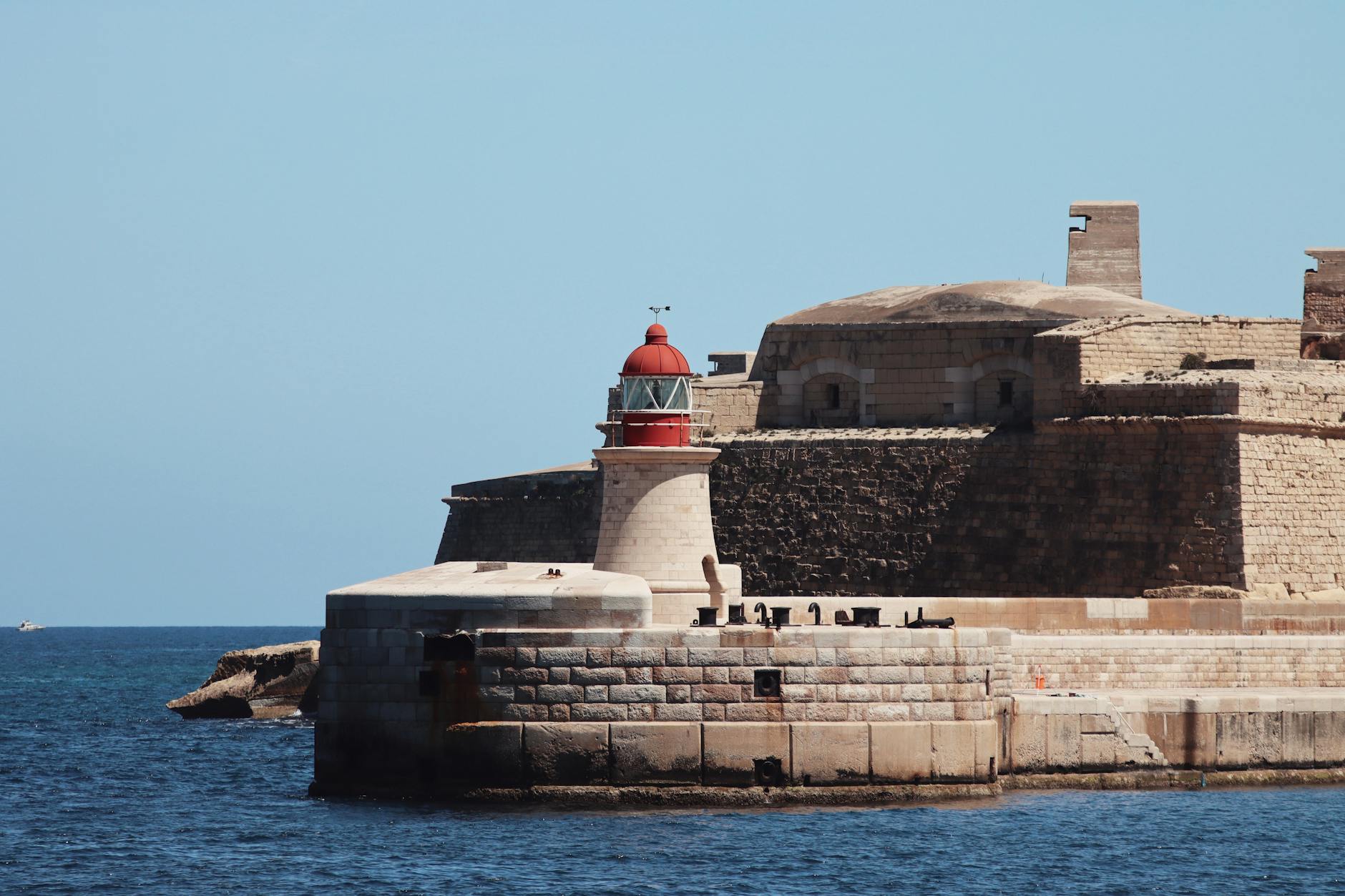 A striking lighthouse stands by ancient fortifications on the seaside at Valletta, Malta.
