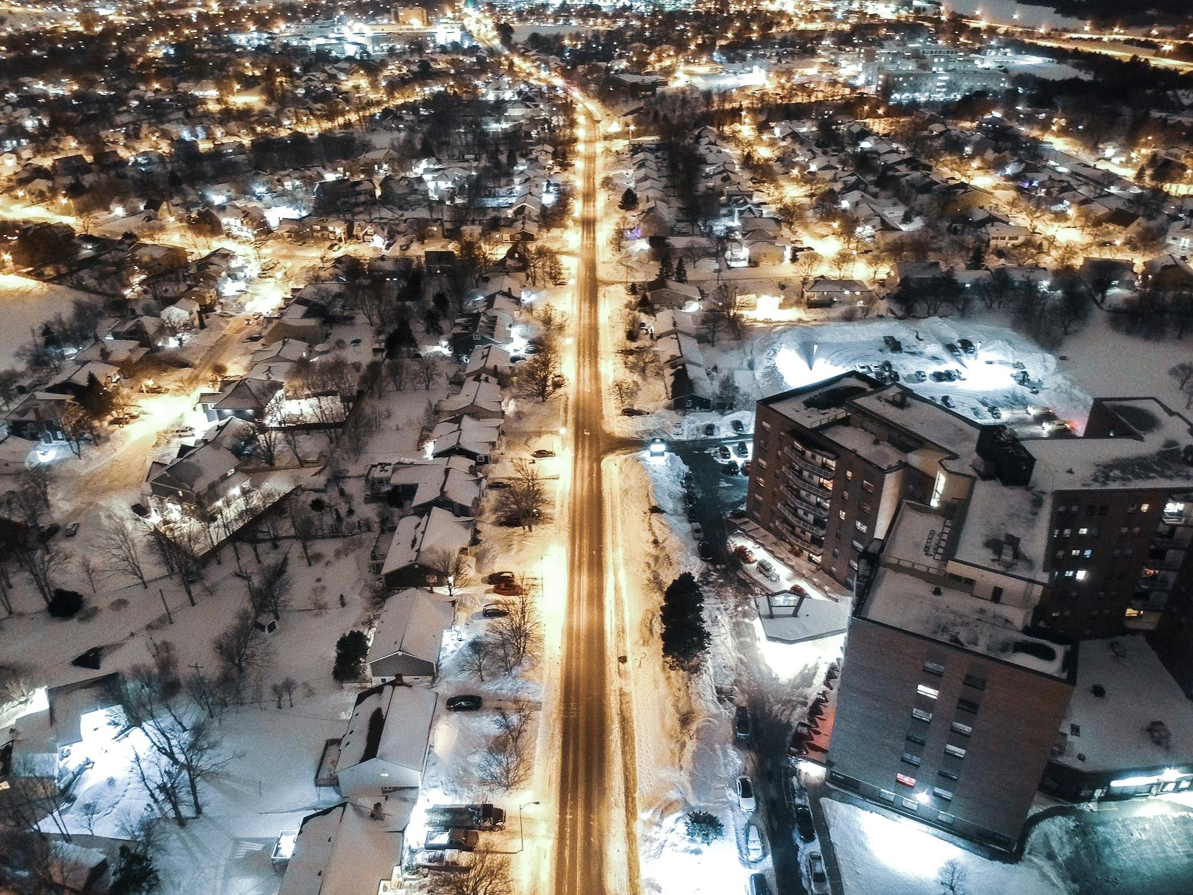 Breathtaking aerial view of a city at night, covered in snow and illuminated by streetlights.