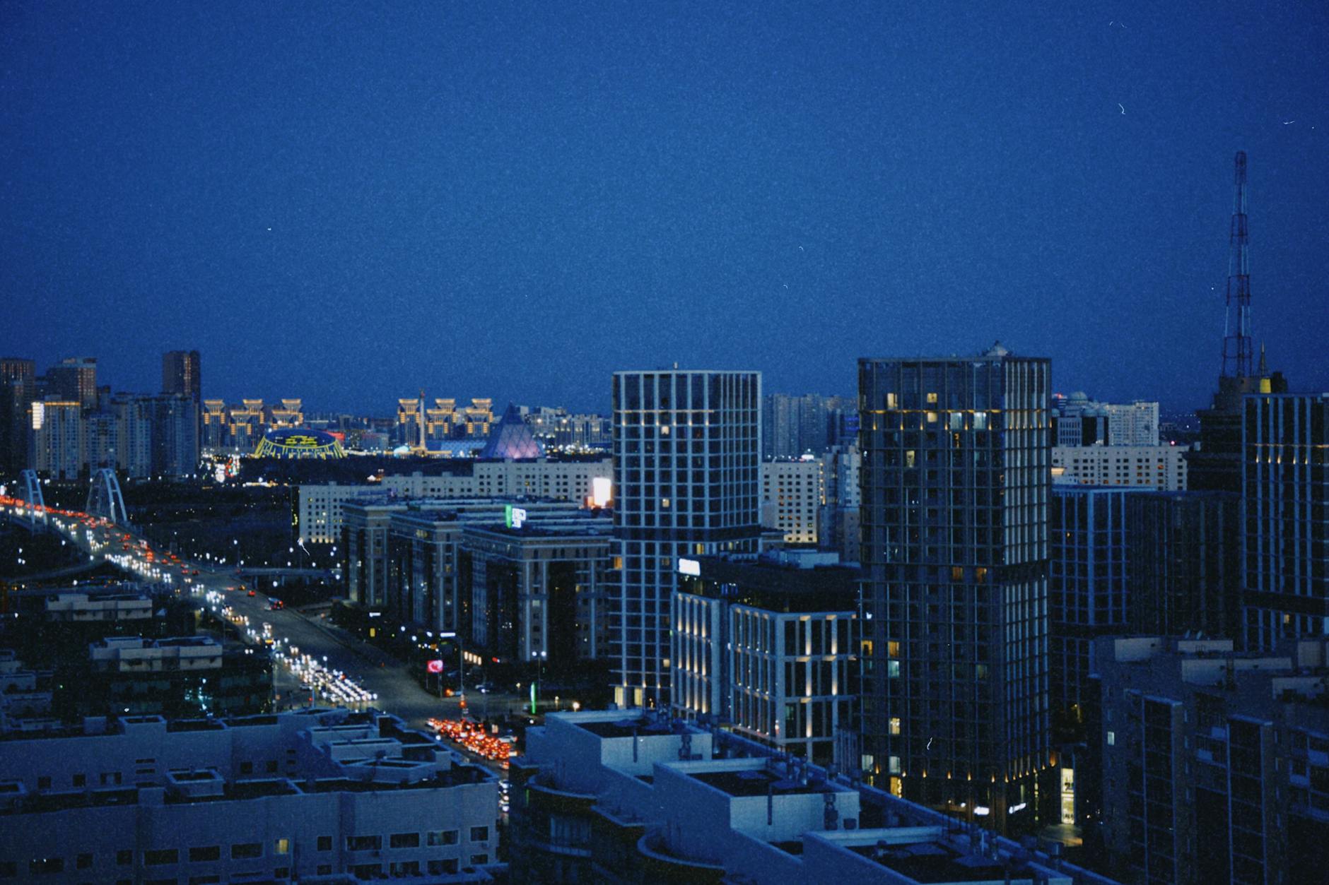 A vibrant night view of Astana, Kazakhstan, featuring modern skyscrapers and city lights.