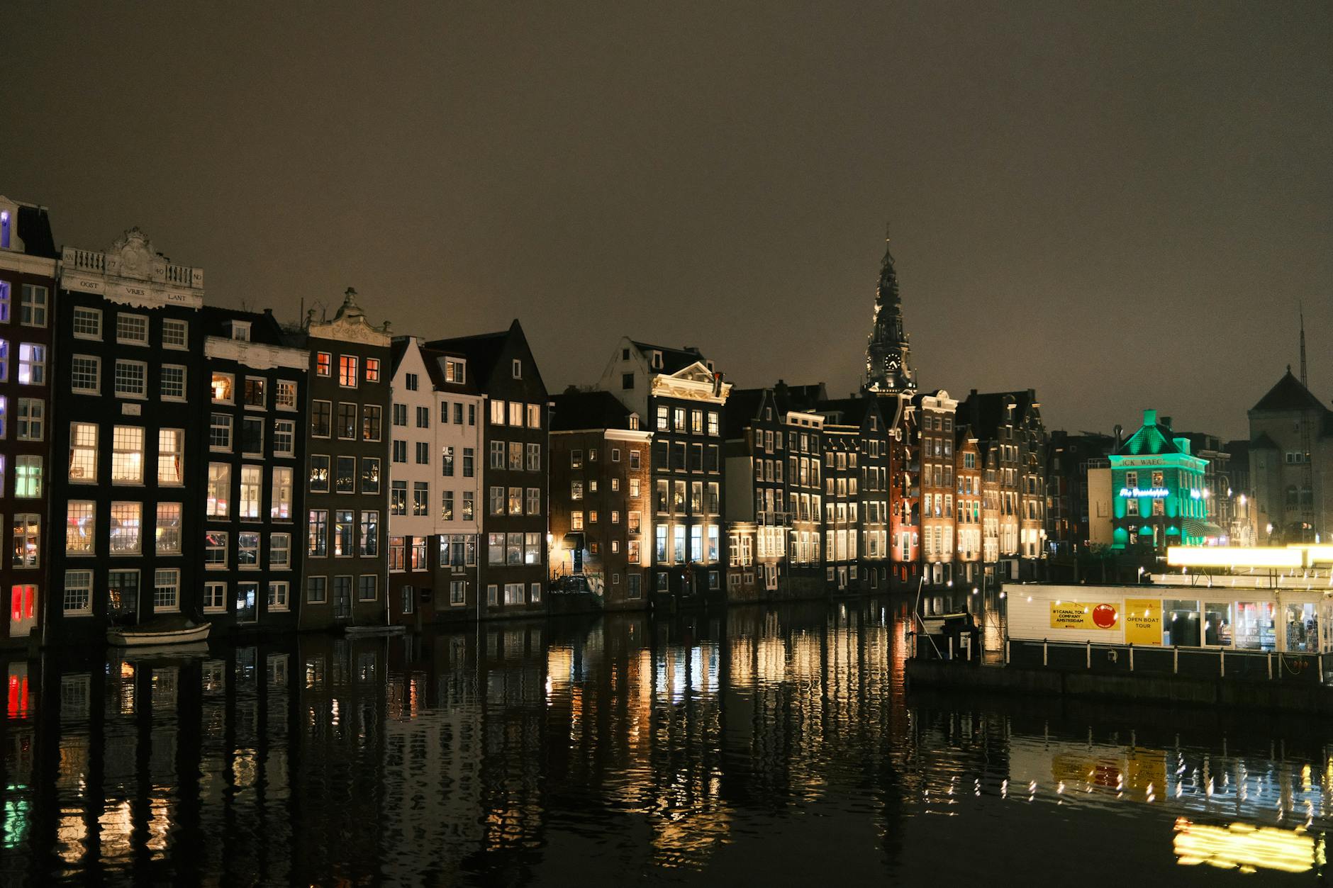 Scenic nighttime view of Amsterdam's iconic canal houses reflecting on water, showcasing Dutch architecture.