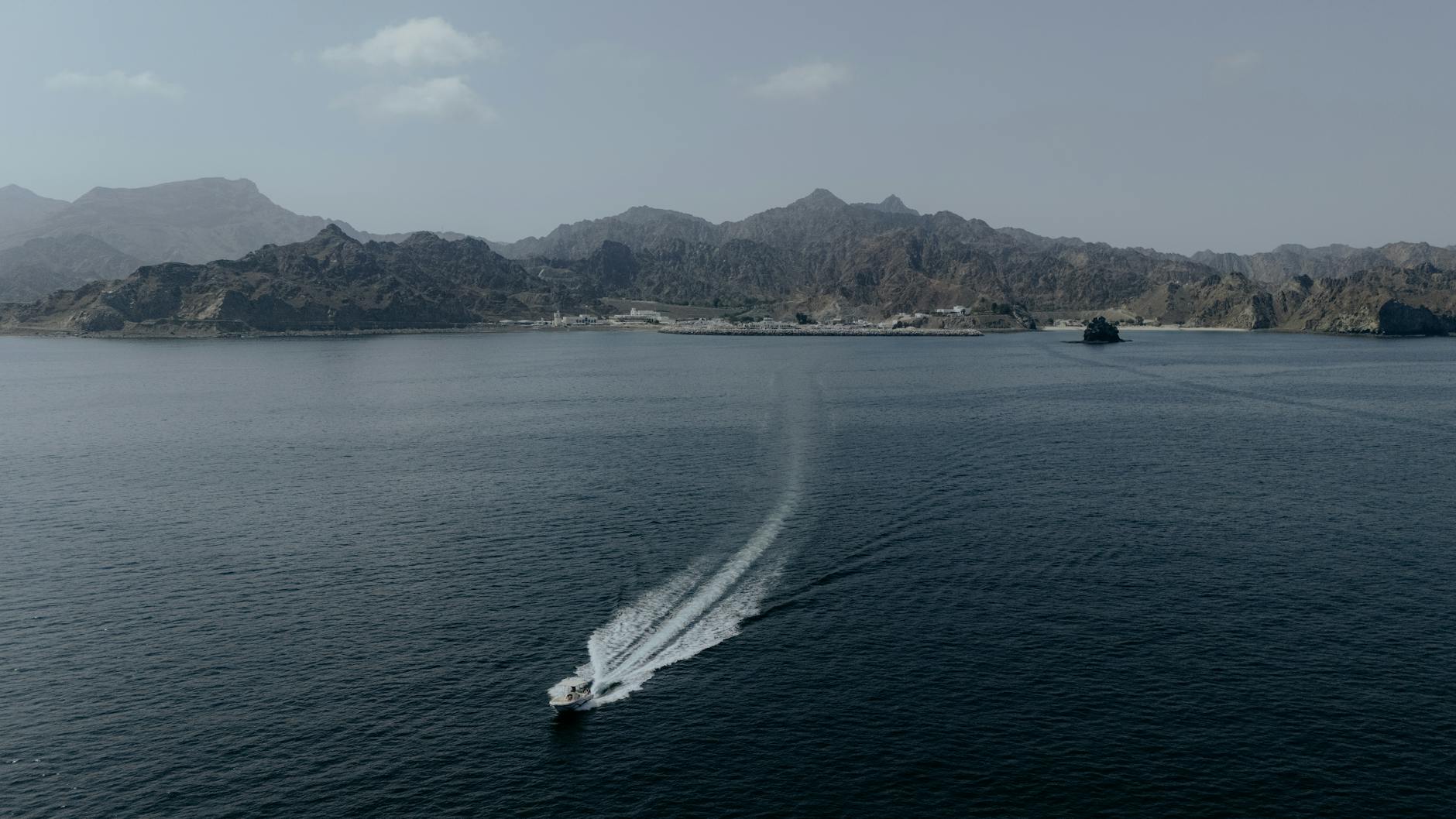 Aerial view of a boat navigating the waters near Muscat, Oman, with mountains in the background.