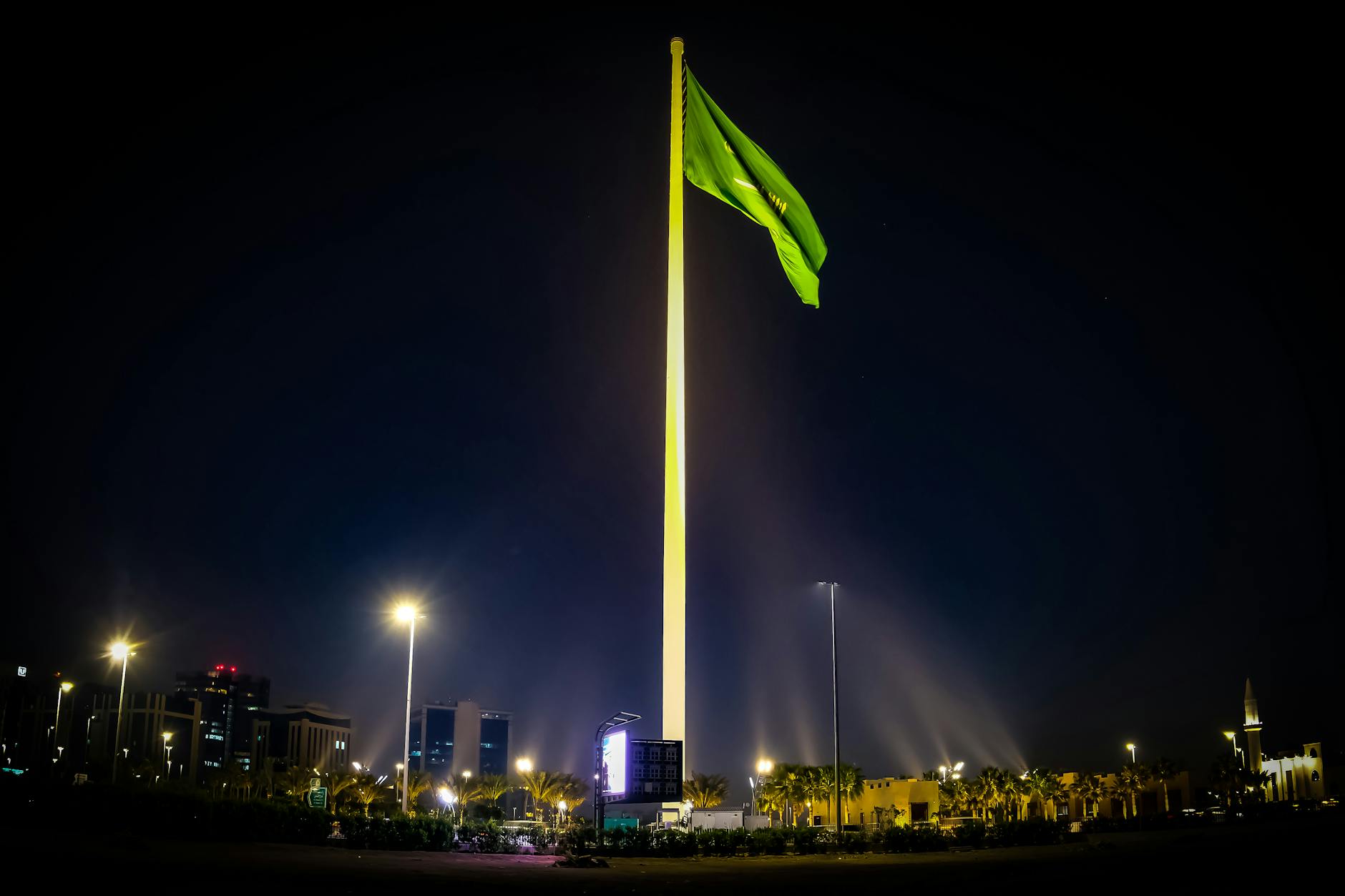 Majestic Saudi Arabian flag illuminated against the night sky, surrounded by cityscape lights in Riyadh.