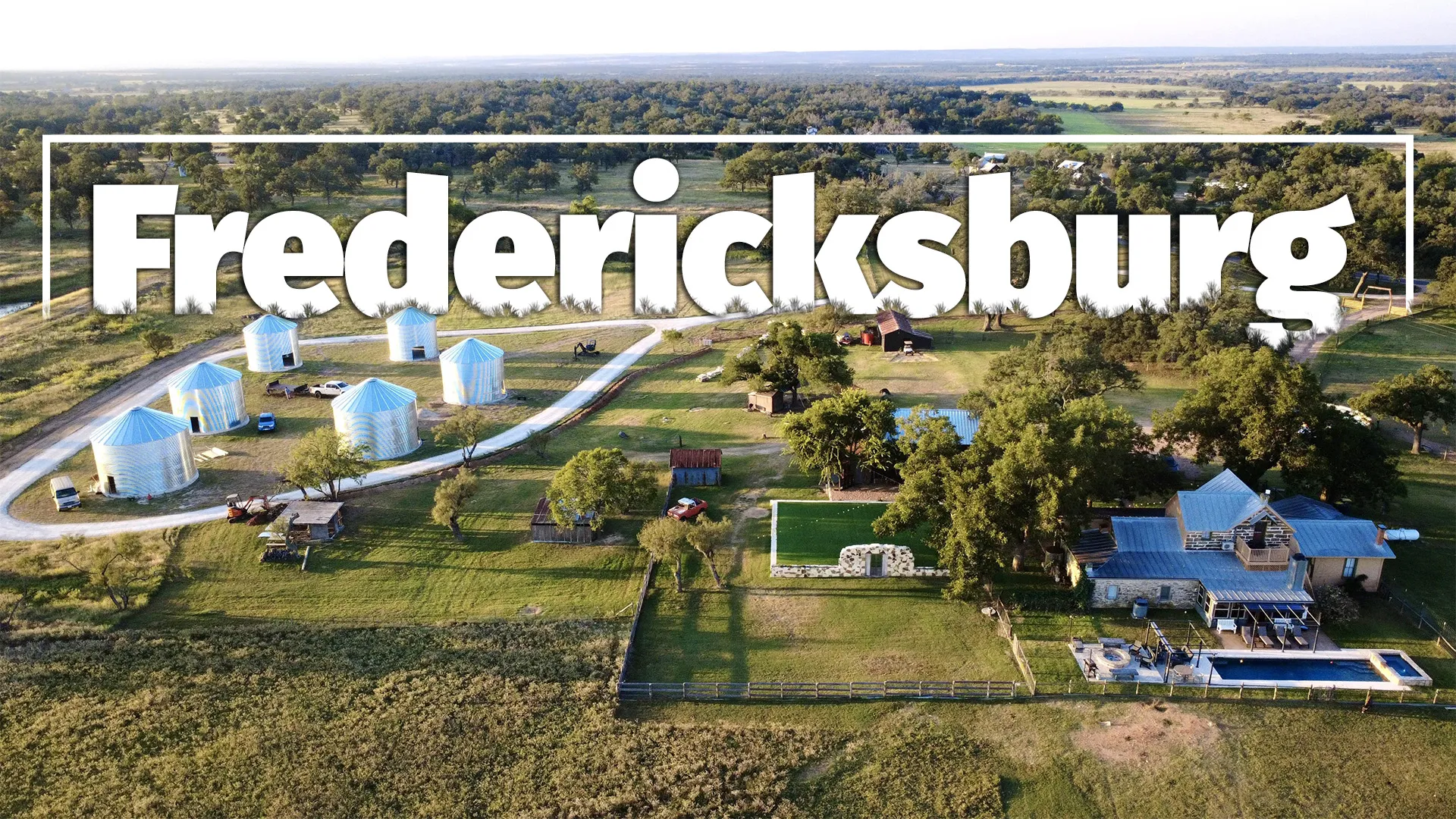 Aerial view of Fredericksburg farmland with grain silos, houses, and agricultural fields along a river.