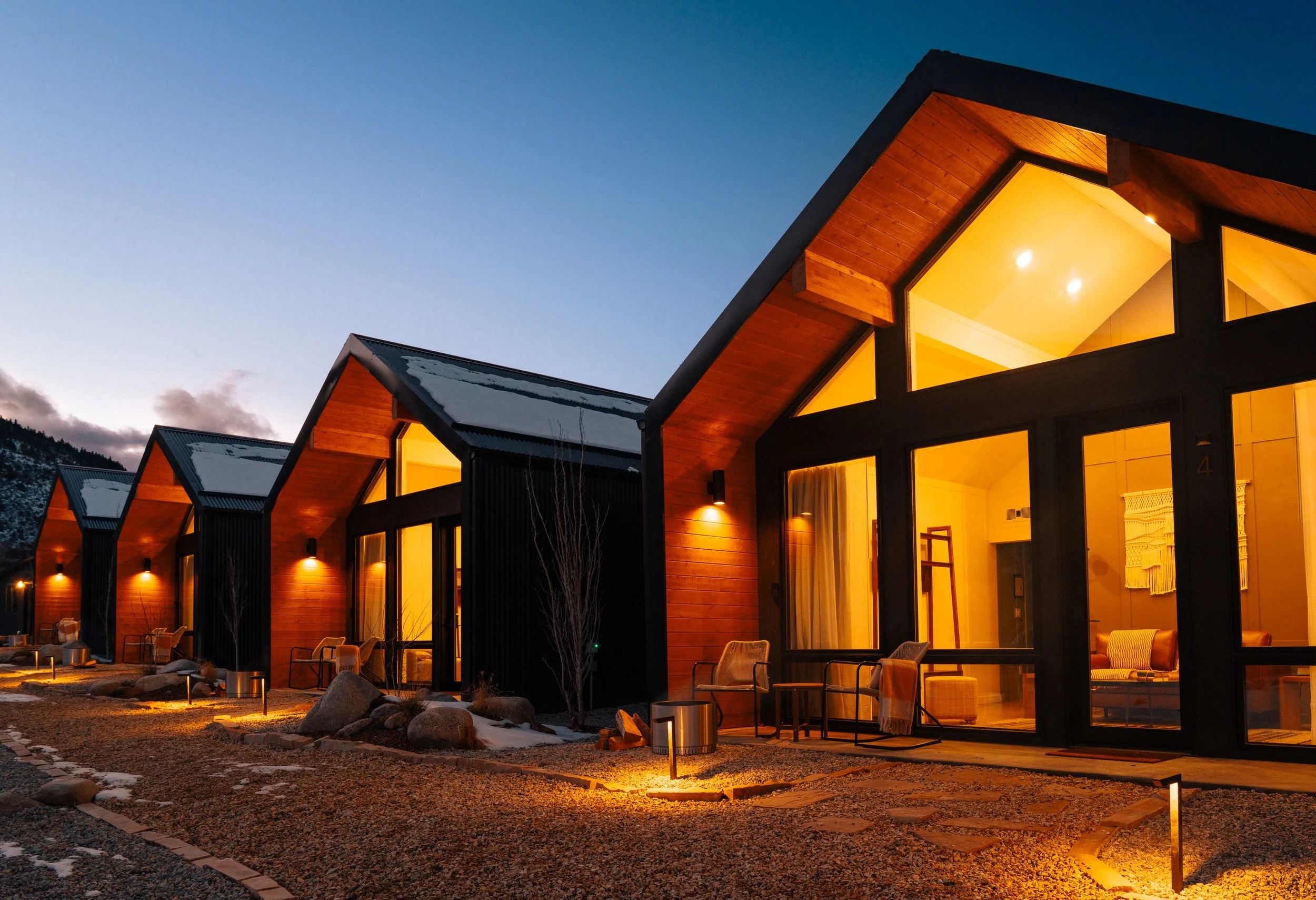 Modern cabins with warm lighting at dusk in mountainous terrain with furnished patios