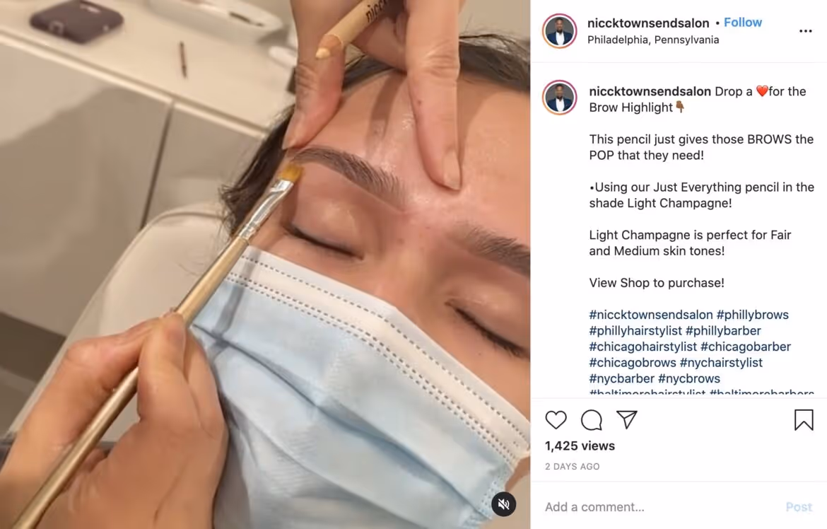 Close-up of an artist applying brow makeup with a small brush on a masked person’s eyebrow.