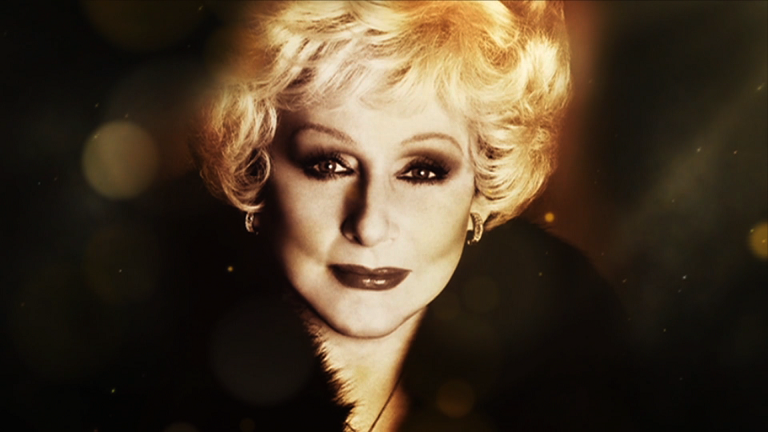 Portrait of a woman with short blonde hair, dark eye makeup, wearing earrings and a fur collar.