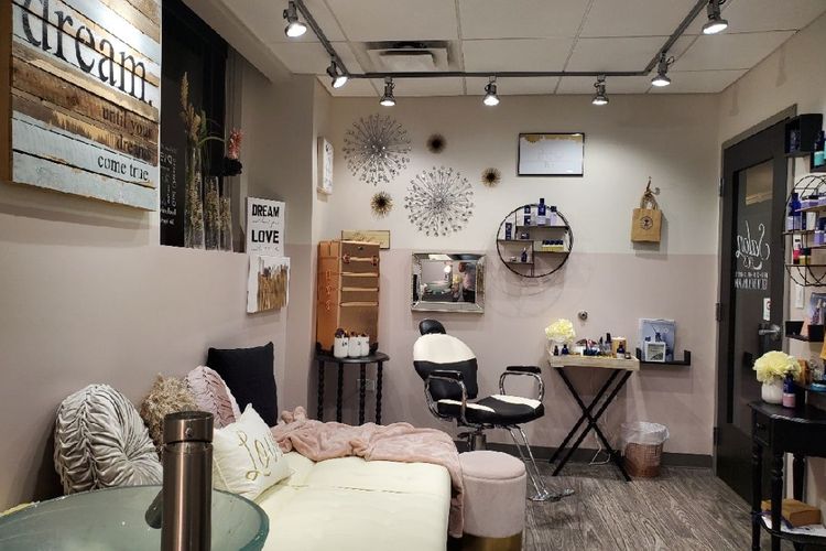 Cozy salon waiting area with cushioned bench, styling chair, and beauty products on shelves and tables.