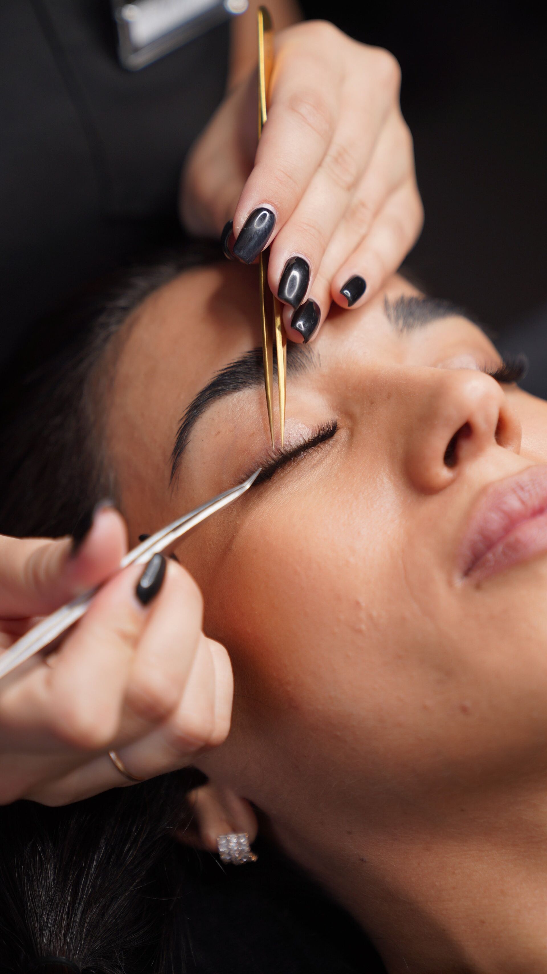 Close-up of a person receiving eyelash extensions from a technician with tweezers.