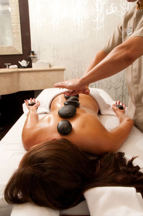 Person receiving hot stone massage with therapist applying pressure on back in a spa room.