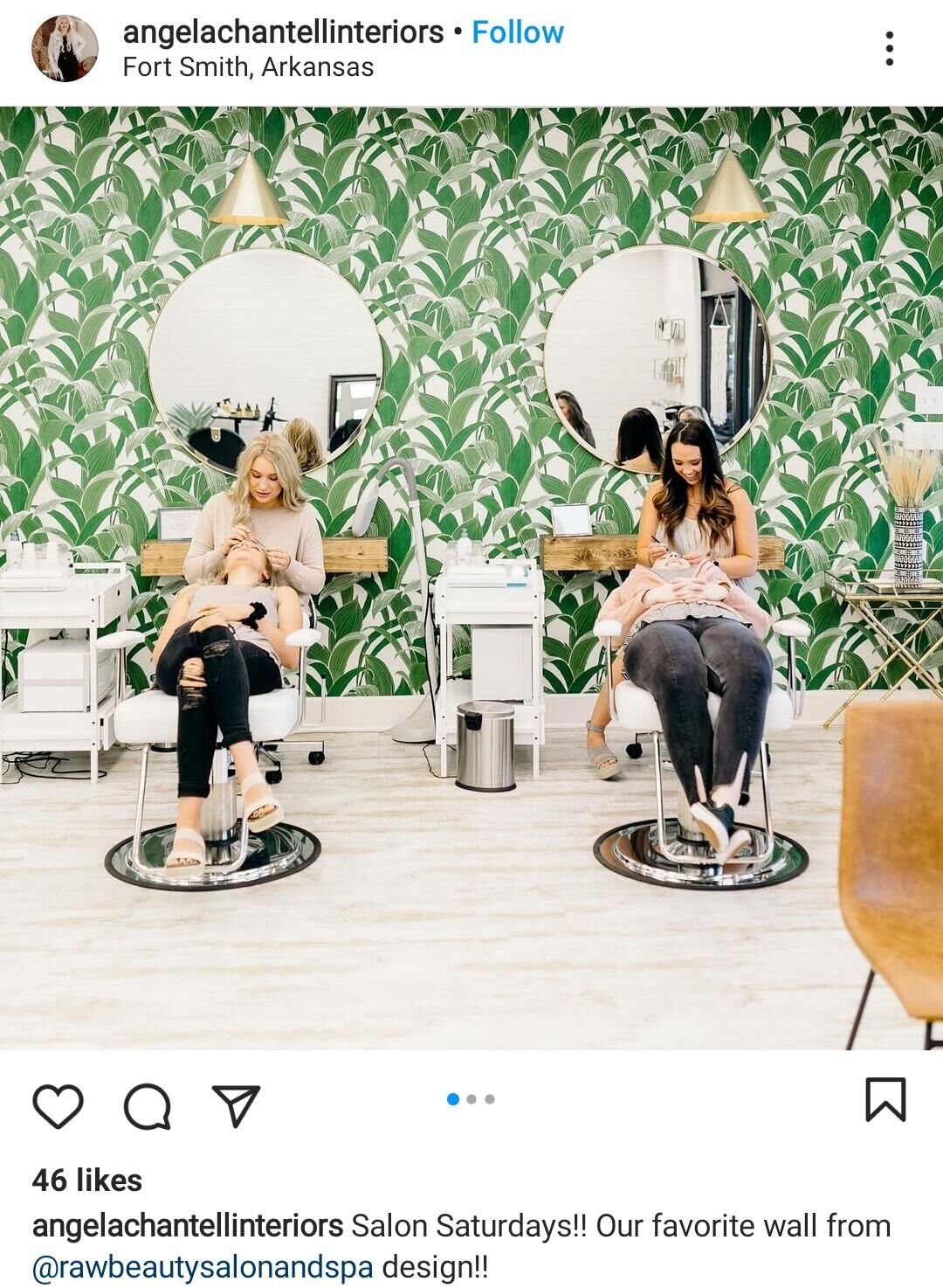 Two women receiving eyelash treatments in a salon with green leafy wallpaper and round mirrors.