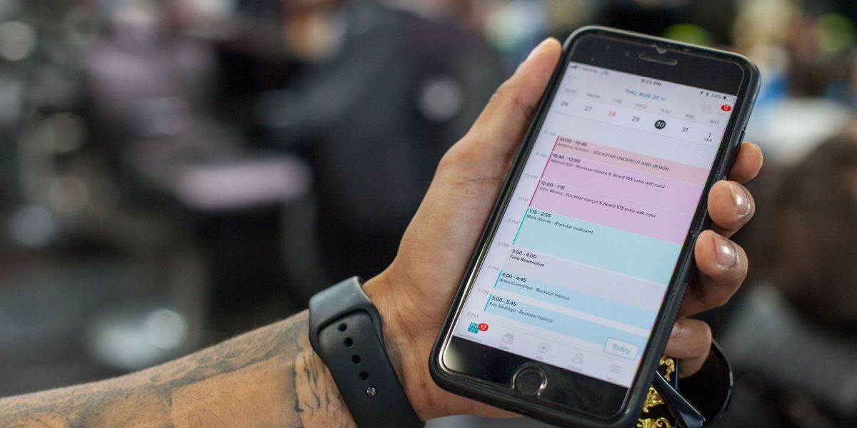 Hand holding smartphone displaying a daily schedule with appointments and time slots in a calendar app.