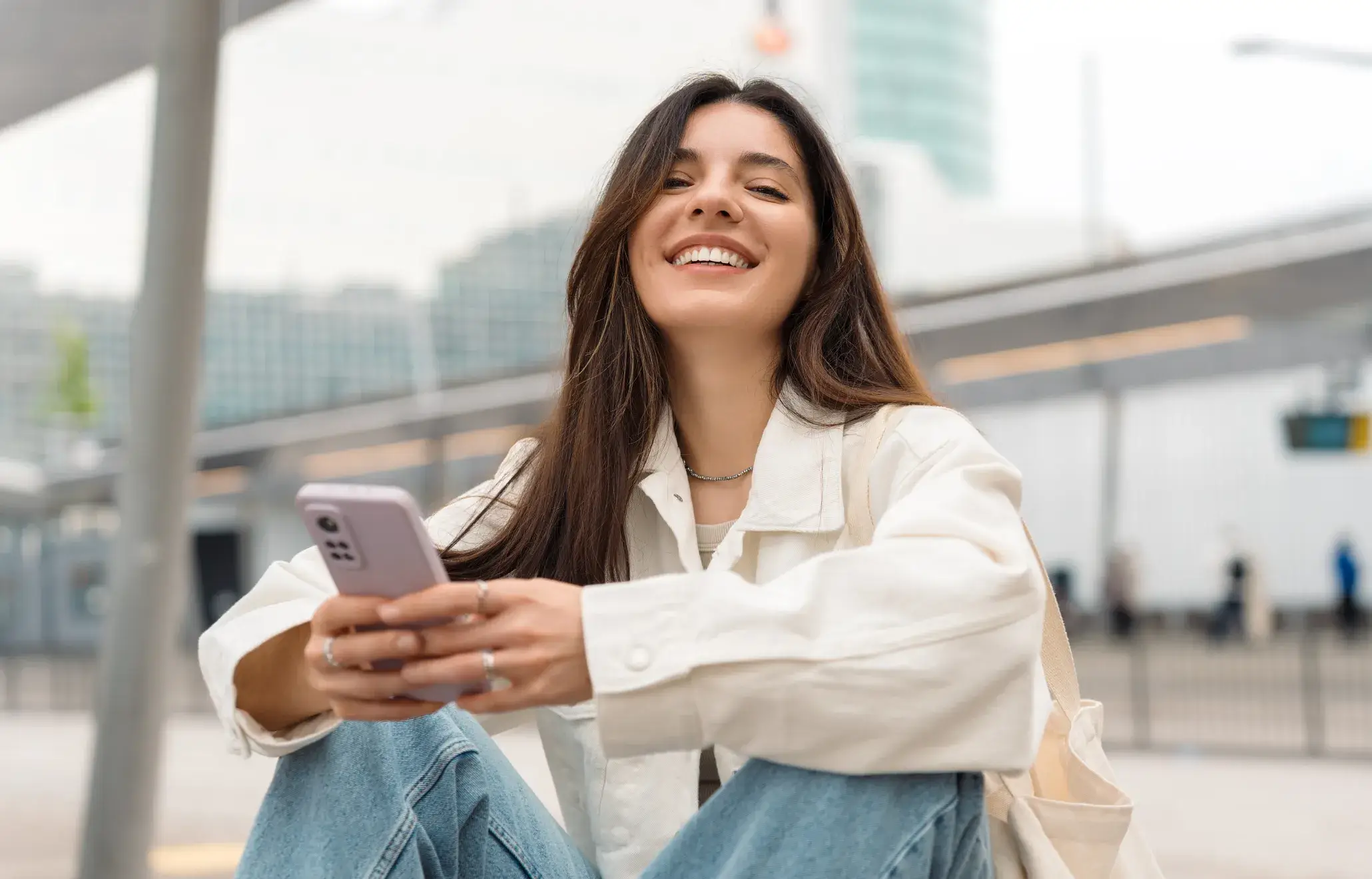 A woman sitting on the ground looking at her cell phone.