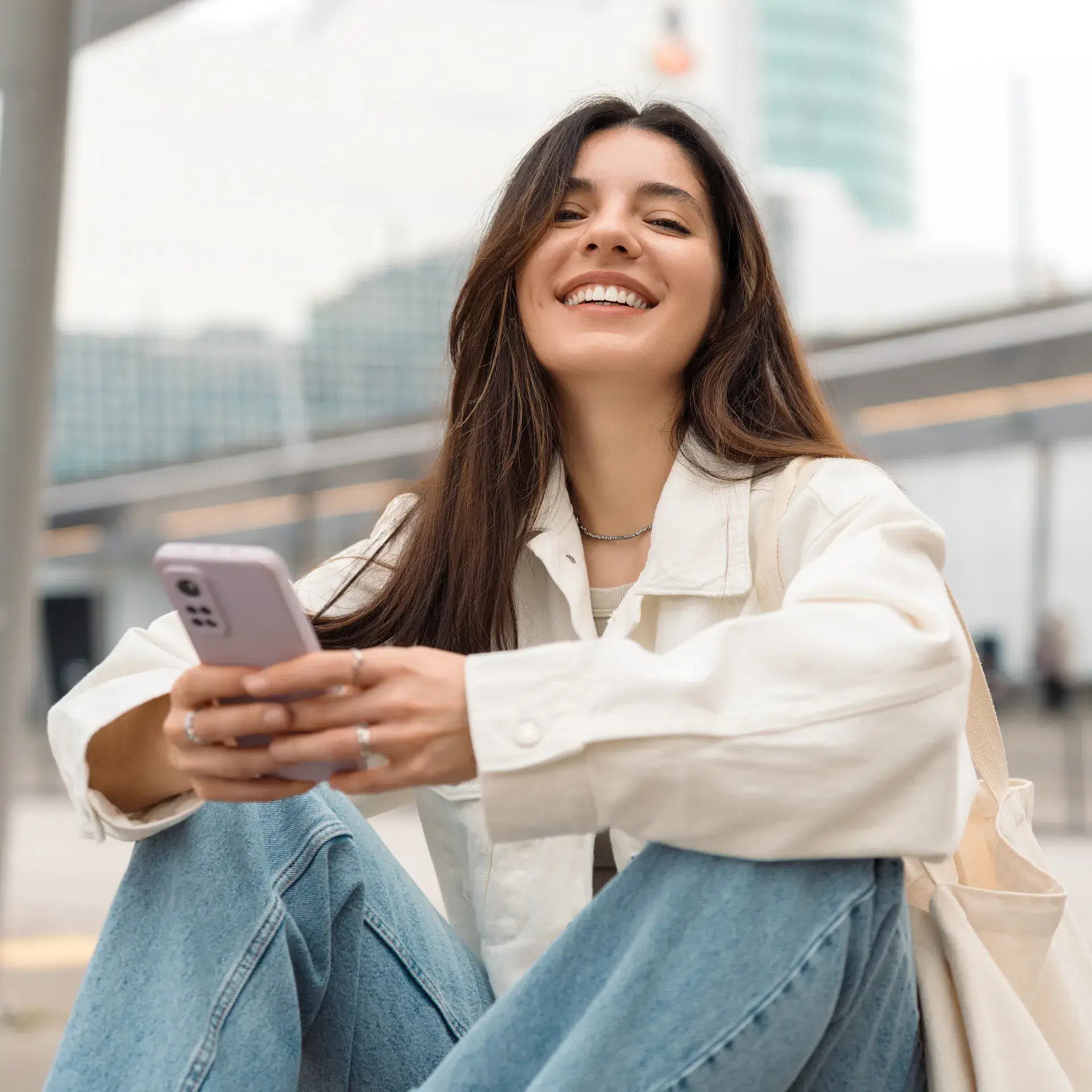 A woman sitting on the ground looking at her cell phone.