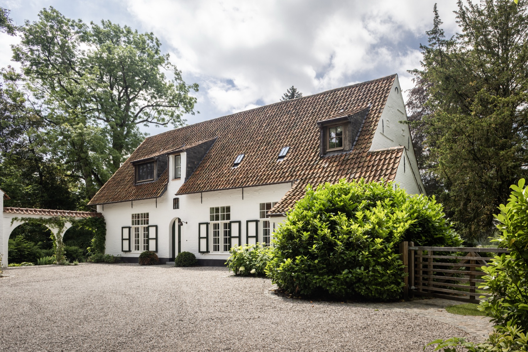 Vooraanzicht van het gerenoveerde landhuis met witte gevel en bogenpartij
