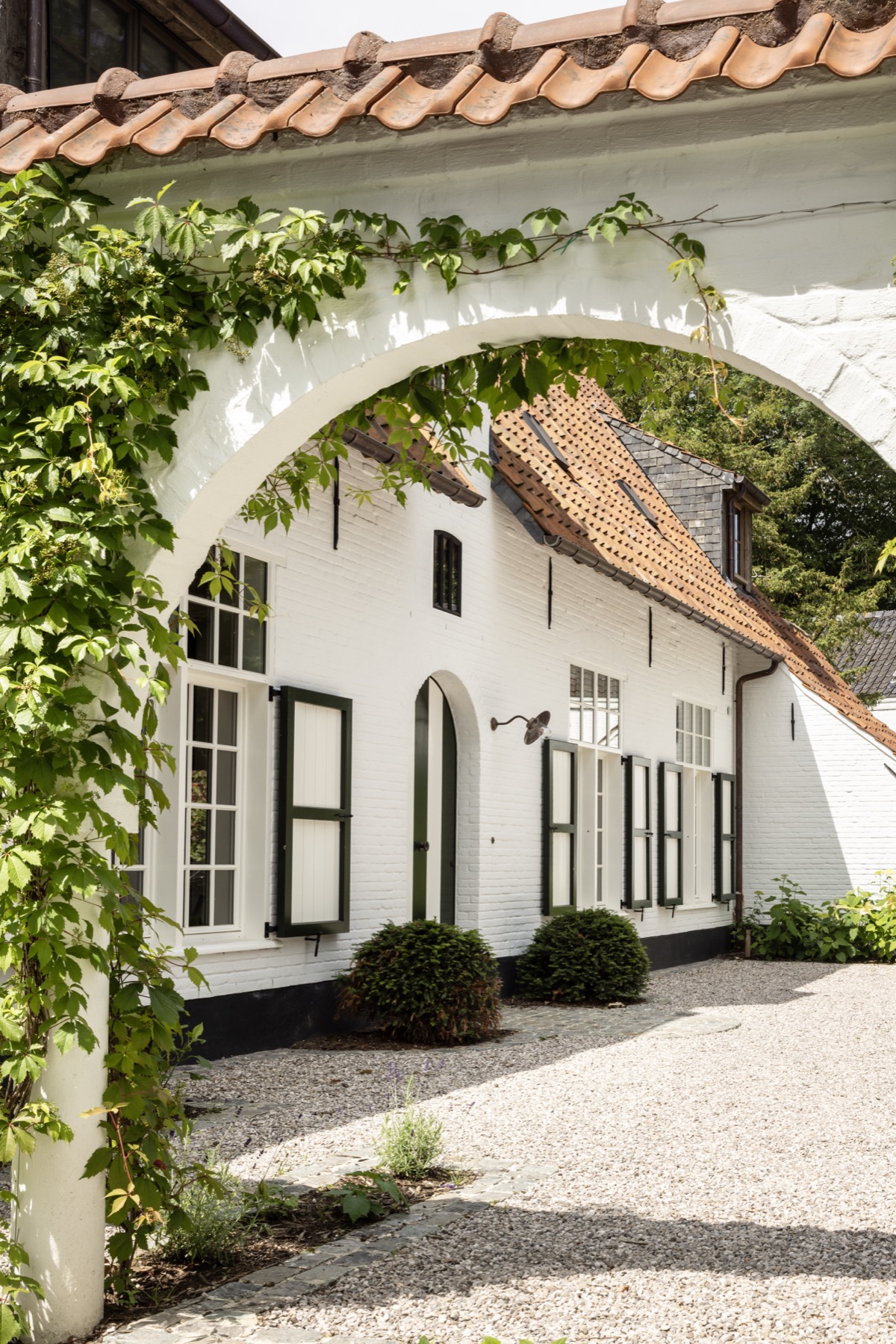 Doorkijk door een begroeide boog naar de woning