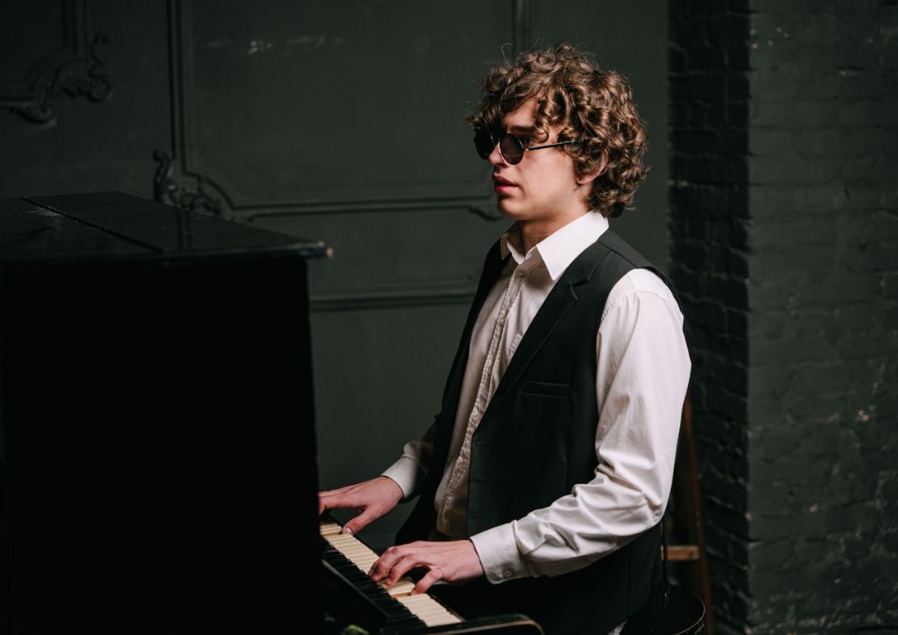 An elegant gentleman, visually impaired, wearing a suit and glasses, gracefully playing the piano.