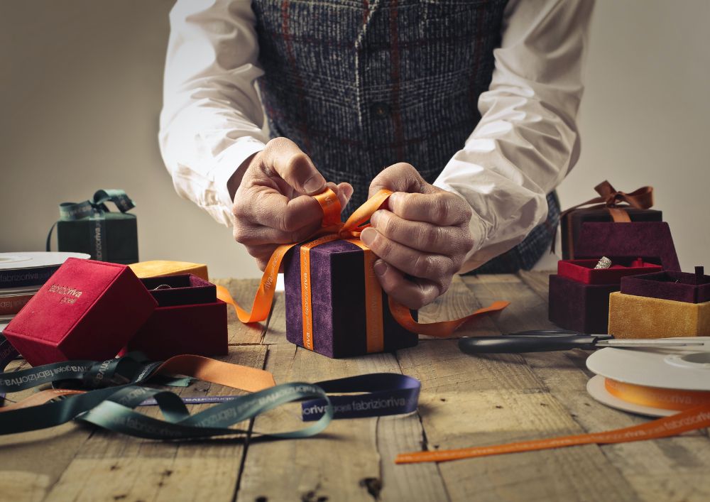 A man carefully ties a ribbon on a gift box, adding a final touch of elegance and thoughtfulness.