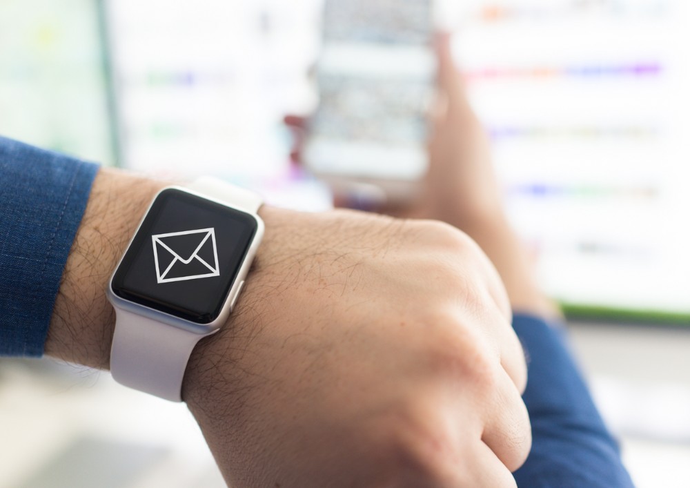 A person holding an Apple Watch that speaks, featuring an email icon on its screen.