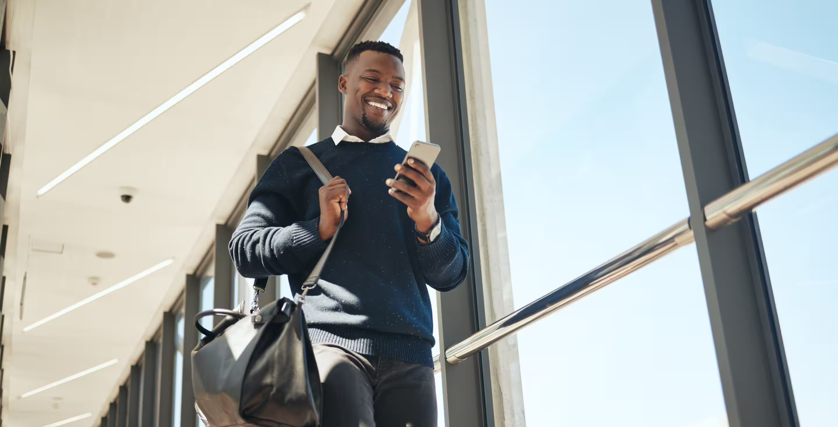 Mann läuft durch einen Flughafen und schaut lächelnd auf sein Handy