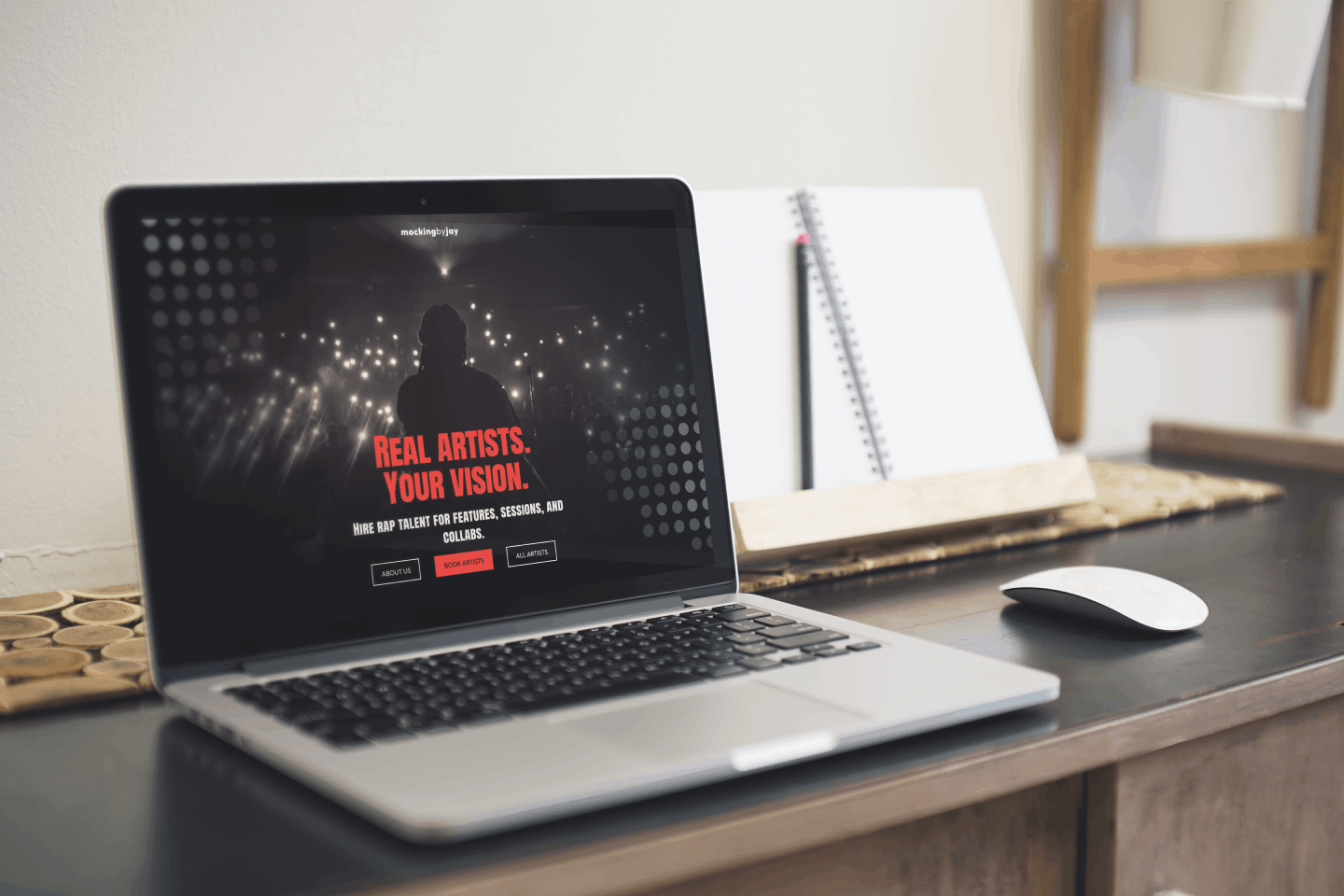 Laptop on desk displaying a hero section with the text 'REAL ARTISTS. YOUR VISION.' and buttons labeled About Us, Book Artists, and All Artists.