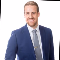 Smiling man with light brown hair wearing a blue suit, white shirt, and gray tie with a tie clip.