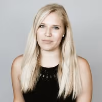 Blonde woman with straight hair wearing a sleeveless black top, posing against a gray background.