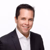 Smiling man with short dark hair wearing a dark suit jacket and white shirt against a white background.