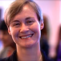 Smiling person with short light brown hair in a softly lit indoor setting.