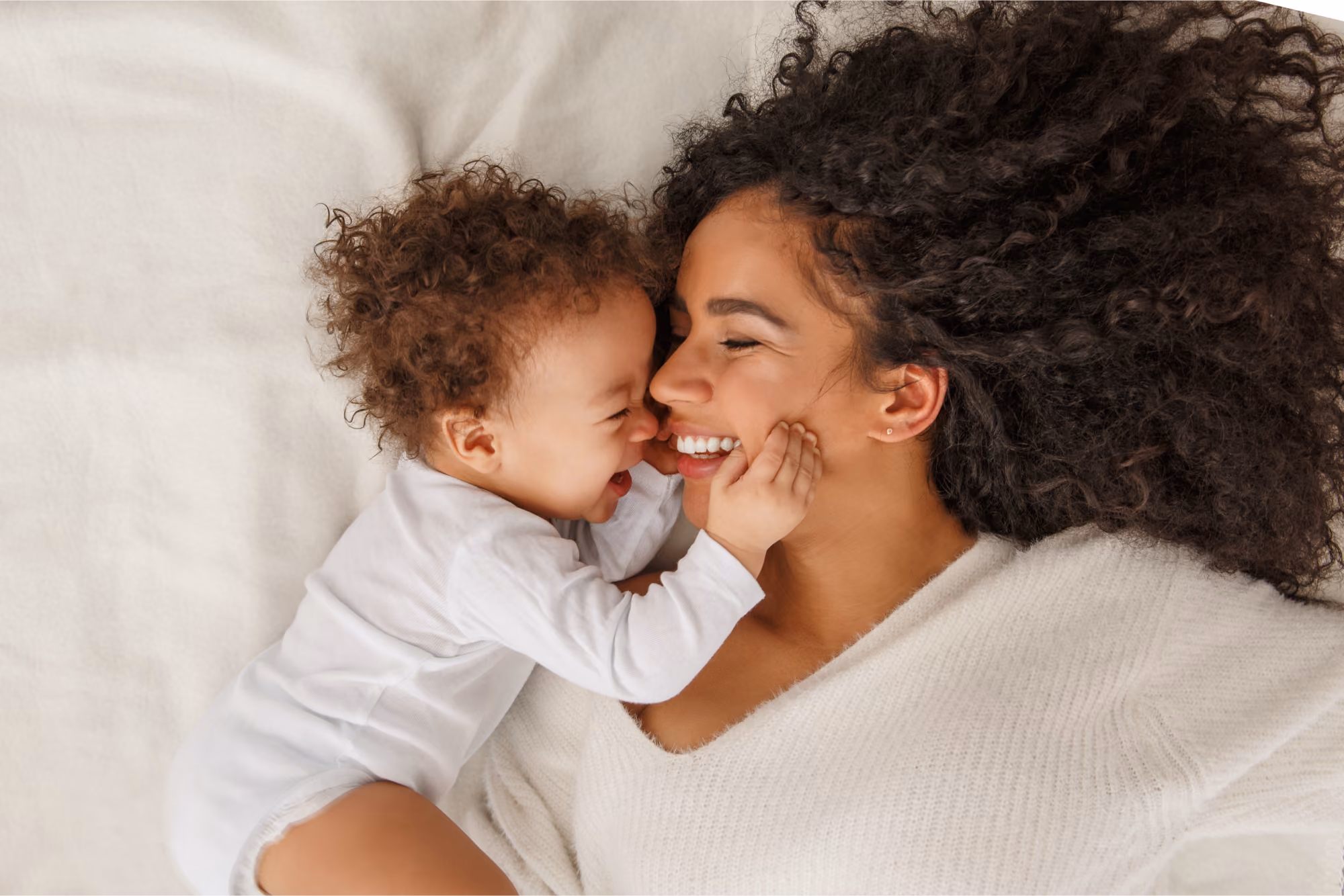 Joyful mother lying down and laughing with her happy baby. Representing a supportive maternity care journey enhanced by the Eve Digital Maternity Platform from Medicity.