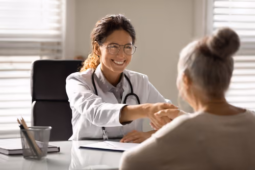 A healthcare professional smiling and shaking hands with a patient, highlighting strengthened clinician-patient satisfaction, improved outcomes and care delivery.